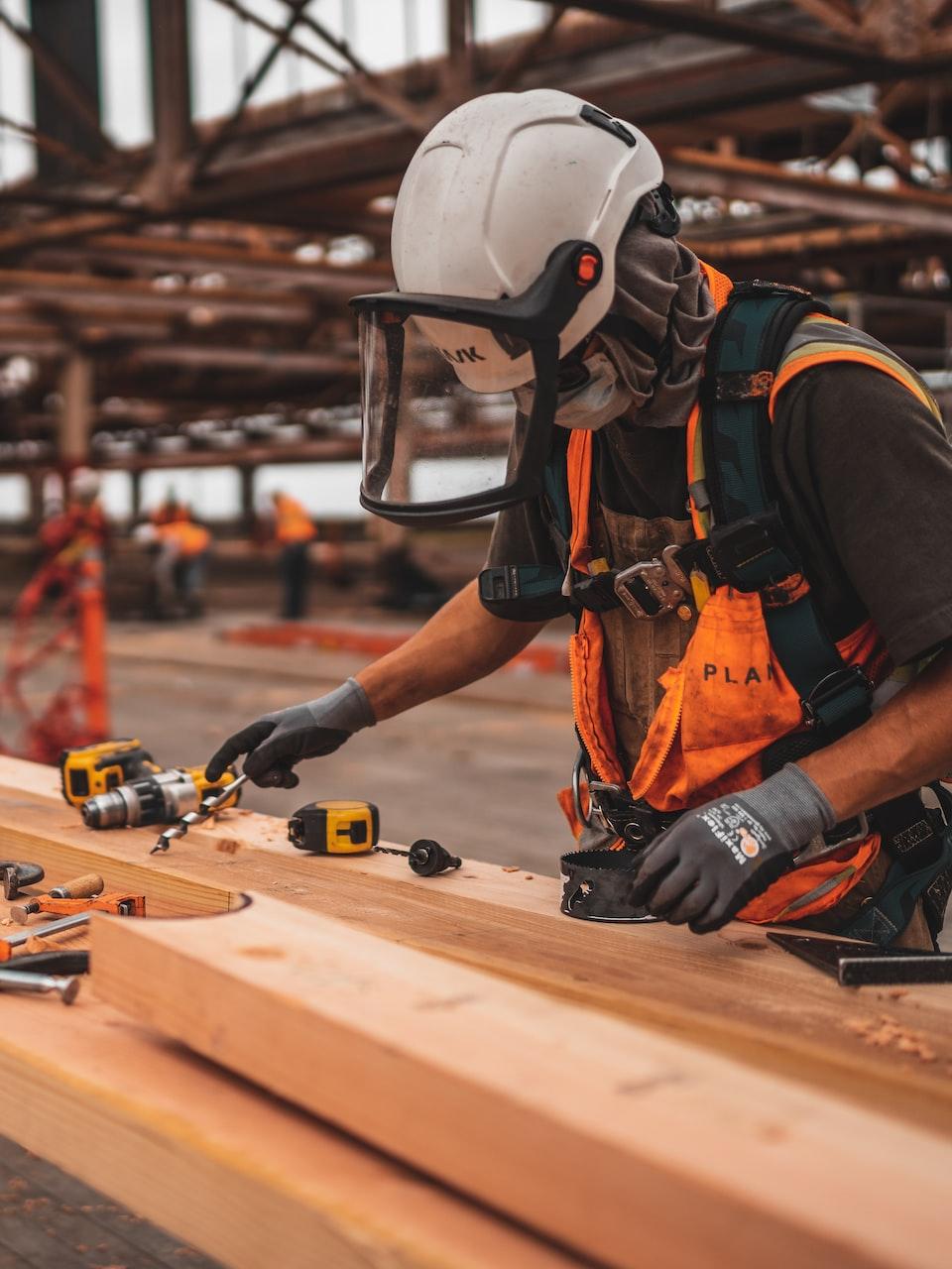 man in orange and black vest wearing white helmet holding yellow and black power tool